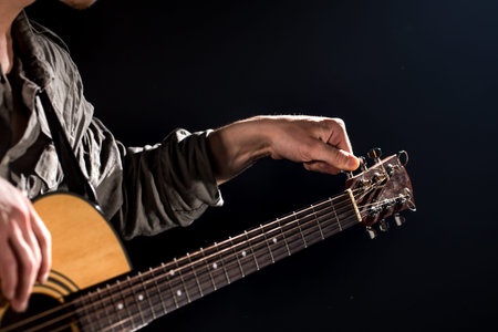 Guitarist, music. A young man plays an acoustic guitar on a black isolated background. Pointed light