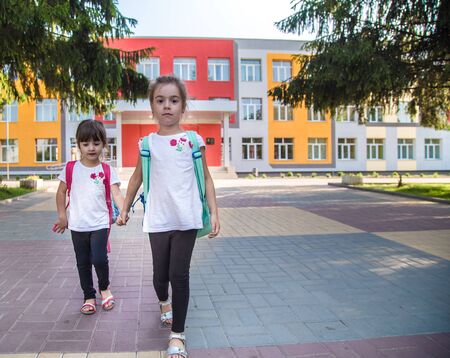 Back to school education concept with girl kids, elementary students, carrying backpacks going to class on school first day holding hand in hand together walking up building stair happilyの写真素材