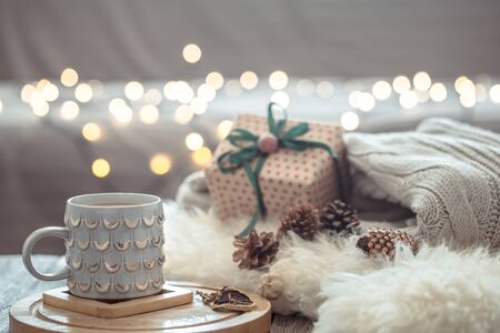 Coffee cup over Christmas lights bokeh in home on wooden table with sweater on a background and present. Winter mood, holiday decoration, magic Christmas.の写真素材
