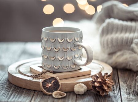 Coffee cup over Christmas lights bokeh in home on wooden table with sweater on a background and decorations. Winter mood, holiday decoration, magic Christmas.の写真素材