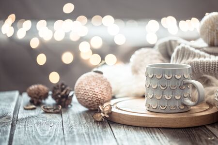 Coffee cup over Christmas lights bokeh in home on wooden table with sweater on a background and decorations. Winter mood, holiday decoration, magic Christmas.の写真素材