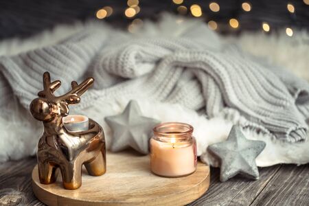 Christmas festive background with toy deer, blurred background with golden lights and candles, festive background on wooden deck table and winter sweater on backgroundの写真素材