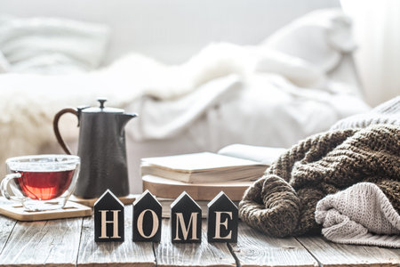 Still life autumn mood in a homely atmosphere with wooden inscription home. A Cup of tea and a kettle on a wooden table near the knitted sweaters .
