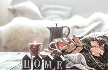 Still life autumn mood in a homely atmosphere with autumn leaves and wooden inscription home. A Cup of tea and a kettle on a wooden table near the knitted sweaters .の写真素材