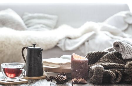 Still life home comfort in the living room with a Cup of tea and a kettle , near a burning candle and a knitted sweater.The concept of home atmosphere and comfortの写真素材
