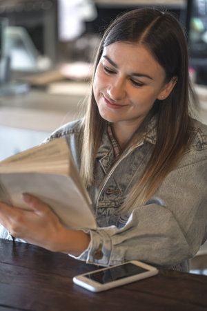 Young girl sitting in cozy cafe and reading a bookの写真素材