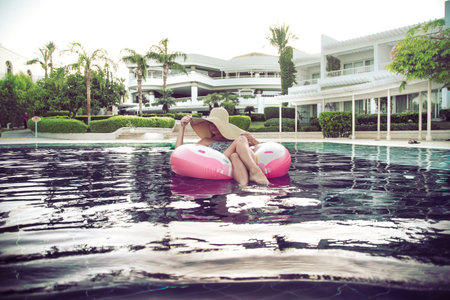 Summer holiday by the pool . A woman in a hat relaxes on an inflatable donut in a blue pool . Summer...