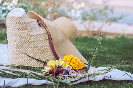 Summer picnic with a plate of tropical fruits . With a stylish wicker bag and a large beach hat . Summer time concept of healthy eating.の写真素材