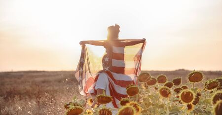 Happy family, dad and daughter holding the American flag at sunset. Dressed in white. The concept of family values and friendship . Patriotic feeling.の写真素材