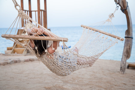 A young woman sits in a hammock by the sea and relaxes. Sea view. The concept of relaxation .