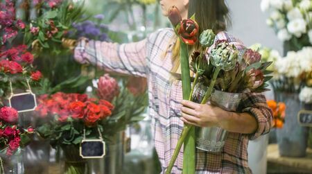 A young girl in a plaid shirt chooses and creates a composition of flowers in a flower shop.の写真素材