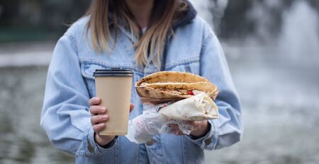 A young woman holding a glass of coffee and fast food. Close up. The concept of fast food .の写真素材