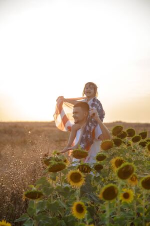 Happy family, dad and daughter holding the American flag at sunset. Dressed in white. The concept of family values and friendship . Patriotic feeling.の写真素材