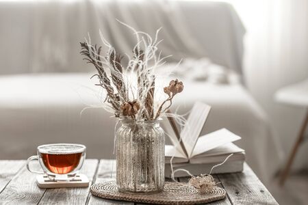 Modern interior. Home decor, beautiful vase with dried flowers, and a Cup of tea in the living room on a wooden table. Vacation spot. The concept of comfort and home decor. Modern style in the interior .の写真素材