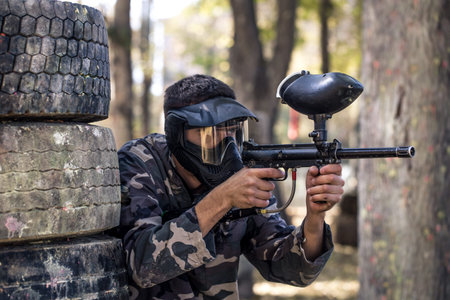 A man with a gun in a uniform and a mask on his face, playing paintball . Sports active games in the...