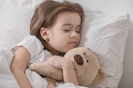 Cute little girl in a white bed sleeping with a soft toy . The concept of children's sleep and development .の写真素材