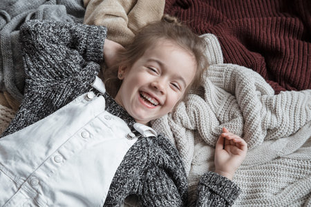 Portrait of an adorable toddler girl wearing fashion knitted clothes. Lies on backdrop of of...