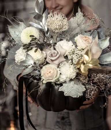 Black pumpkin with a floral arrangement of beautiful flowers in women's hands. The concept of autumn holidays.の写真素材