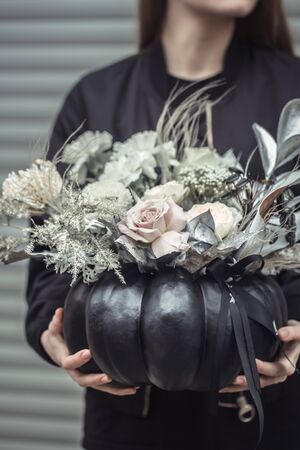 Black pumpkin with a floral arrangement of beautiful flowers in women's hands. The concept of autumn holidays.の写真素材