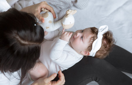 Mom plays with a toy with her newborn daughter, lying on the bed, top view. The concept of motherhood and child development.の写真素材