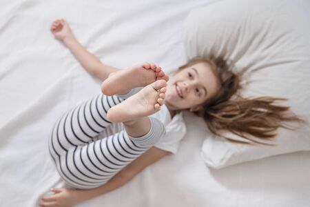 Cute little fun girl with long hair in bed woke up in the morning . Concept of sleep and development of children.