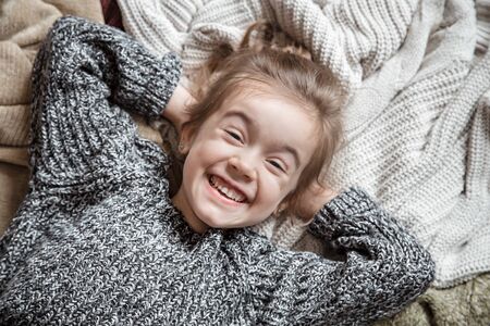 Portrait of an adorable toddler girl wearing fashion knitted clothes. Lies on backdrop of of multiple different cozy knitted sweaters. The concept of warm clothes.の写真素材