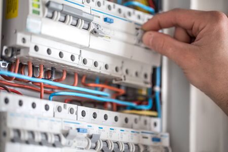 Man, an electrical technician working in a switchboard with fuses. Installation and connection of electrical equipment. Professional with tools in hand. concept of complex work, space for text.の写真素材