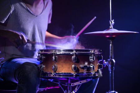 A drummer plays drums on a blue background. Beautiful special effects of light and smoke. The process of playing a musical instrument. The concept of music. Close-up photo.の写真素材