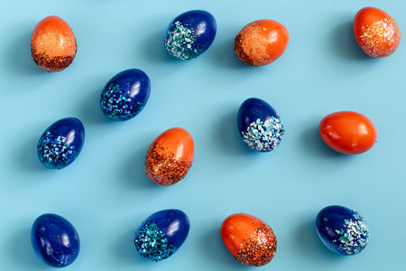 Beautiful Easter blue background with blue and orange decorative eggs in spangles . The concept of...
