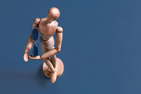 Wooden figure of a man on a blue background with a clock, the concept of object, time and man.の写真素材