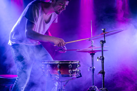 A drummer plays drums on a blue background. Beautiful special effects of light and smoke. The...
