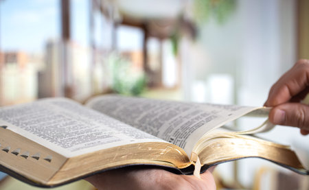 A man holds a Bible and reads a book on the terrace. Morning time. Close up.