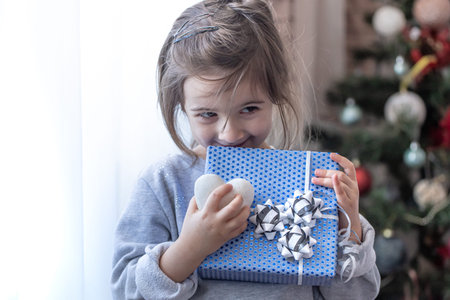 A little girl is holding a blue holiday gift . Concept of holidays.