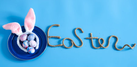 Easter creative inscription on a blue background with items of Easter decor. The concept of the...