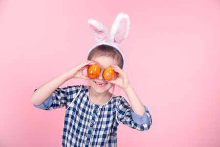 Portrait of a cute little girl with Easter eggs on an isolated pink background. Dressed in a blue...