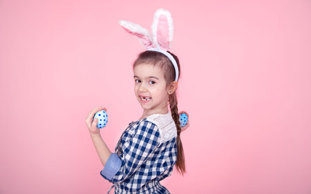 Portrait of a cute little girl with Easter eggs on an isolated pink background. Dressed in a blue...