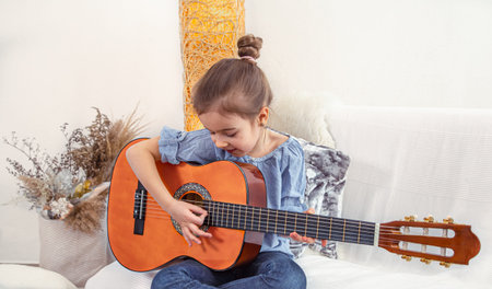A little girl sits on the couch and plays the guitar . Concept of child development and values.