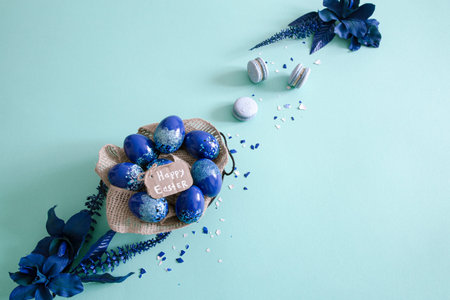 Creative Easter layout made of colorful eggs and flowers on blue background. Circle wreath flat lay...