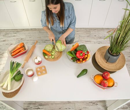 A young beautiful woman is preparing a salad of various vegetables in the kitchen. The concept of a healthy diet and lifestyle.の写真素材