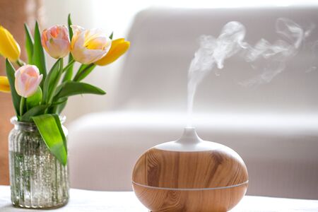 Aroma oil diffuser lamp on the table on a blurred background with a beautiful spring bouquet of tulips.の写真素材