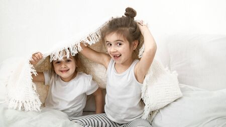Two cute little sister girls are cuddling on the bed in the bedroom. The concept of family values and children's friendship.の写真素材