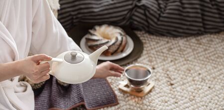 Hands of a young woman pour tea from a teapot. Preparing Breakfast in a cozy home atmosphere.の写真素材