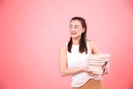 Portrait of a young woman with glasses on a pink background with books in her hands . Concept of...