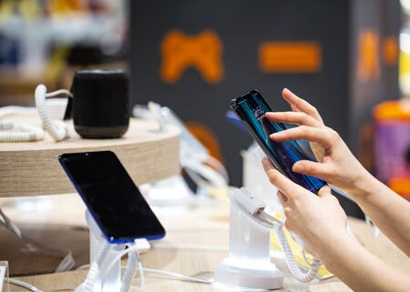 A young woman in the store is standing near the stand and choosing a phone . The concept of shopping.の写真素材