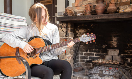 A young woman plays the guitar in a cozy atmosphere. The concept of Hobbies and recreation.