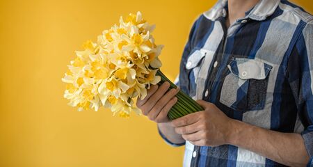 Hipster-a man on a yellow background in a shirt and a large bouquet of daffodils. The concept of greetings and women's day.の写真素材
