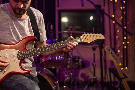 A man plays an electric guitar in a recording Studio. A rehearsal room for musicians with a drum kit in the background. The concept of musical creativity.の写真素材