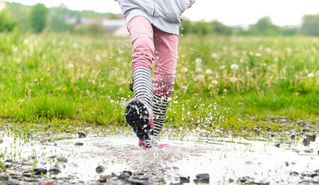 A child in rubber boots jumps in a puddle. Close up. Autumn-summer conceptの写真素材
