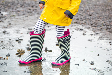 A child in rubber boots jumps in a puddle. Close up. Autumn-summer concept
