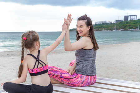 A young mother and daughter in sports clothes, playing sports on the beach by the sea. Family values and a healthy lifestyle.の写真素材